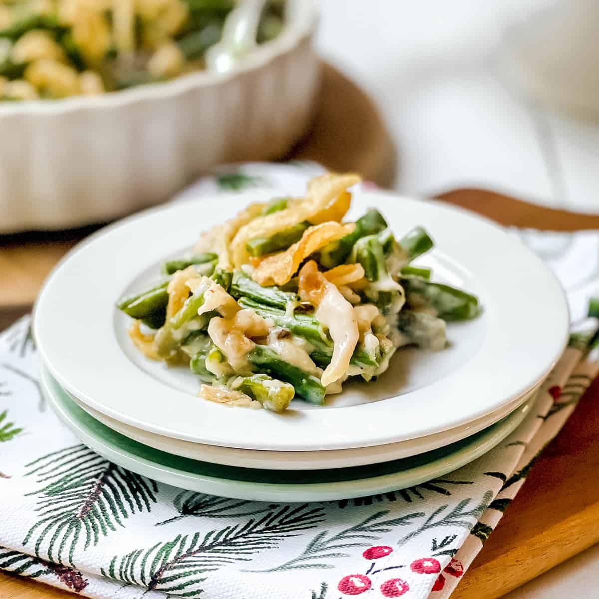 Square image of a serving of green bean casserole on a plate sitting on a festive linen.