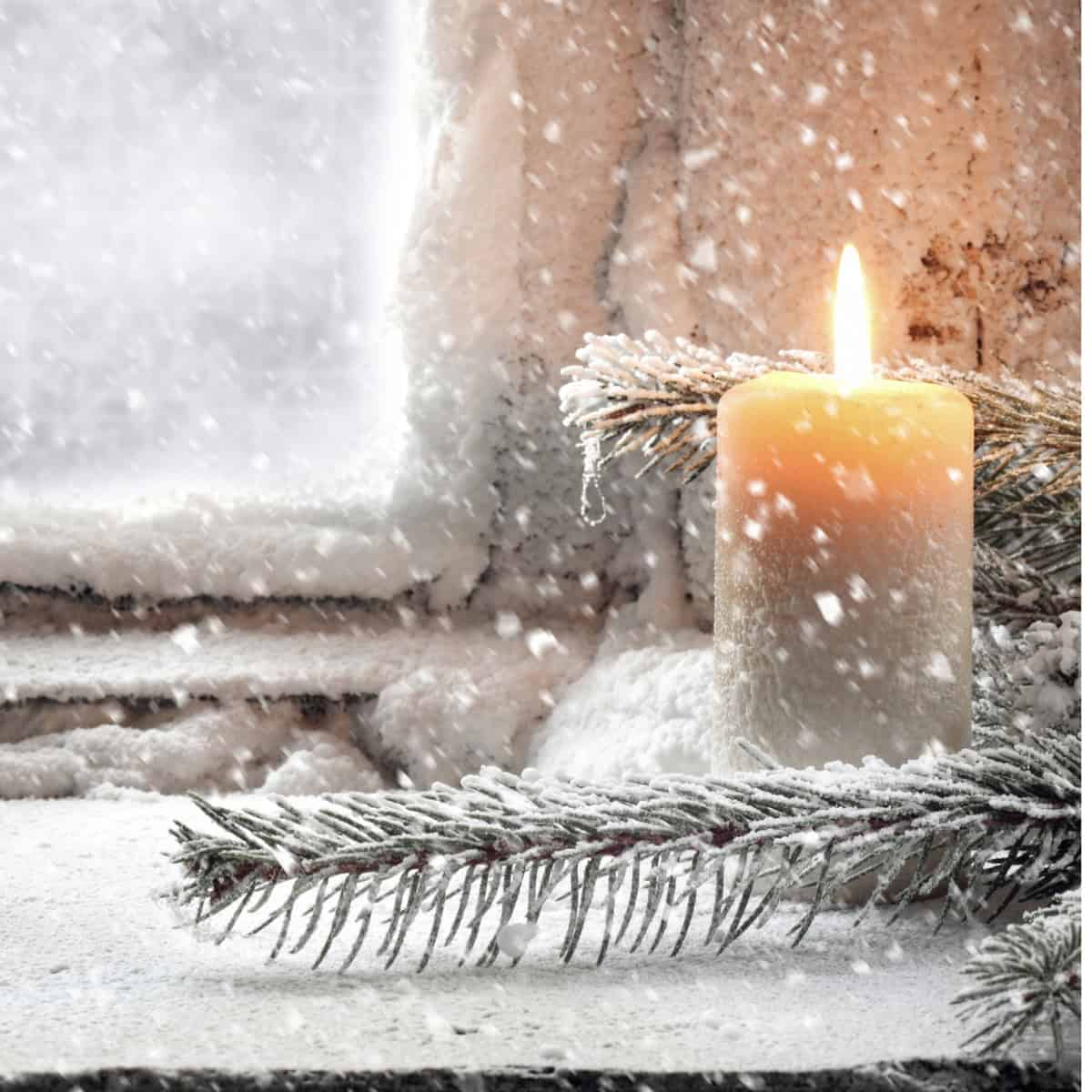 A lit candle sits on a snowy windowsill with evergreen branches, making Christmas memorable as snow falls outside a frosted window.