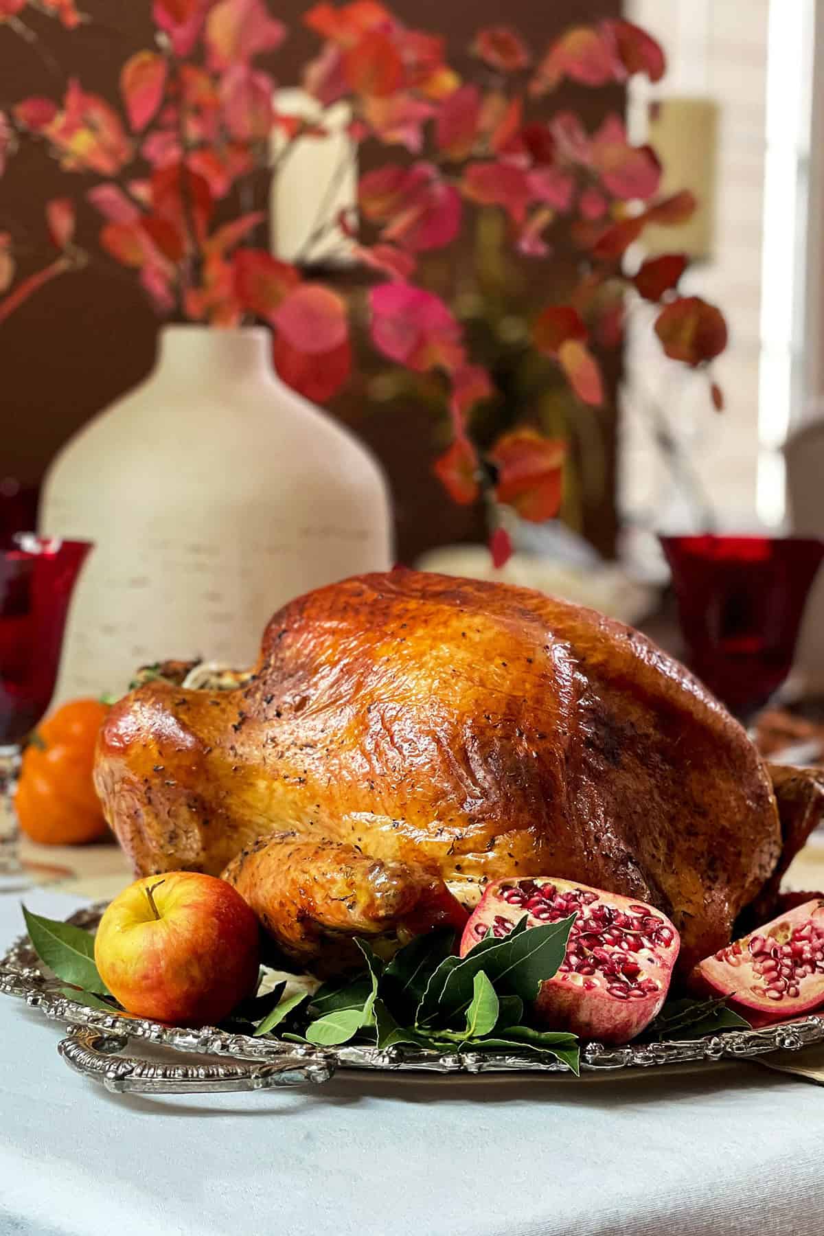 Herb Roasted Turkey on a holiday table ready for carving with place settings in the background.