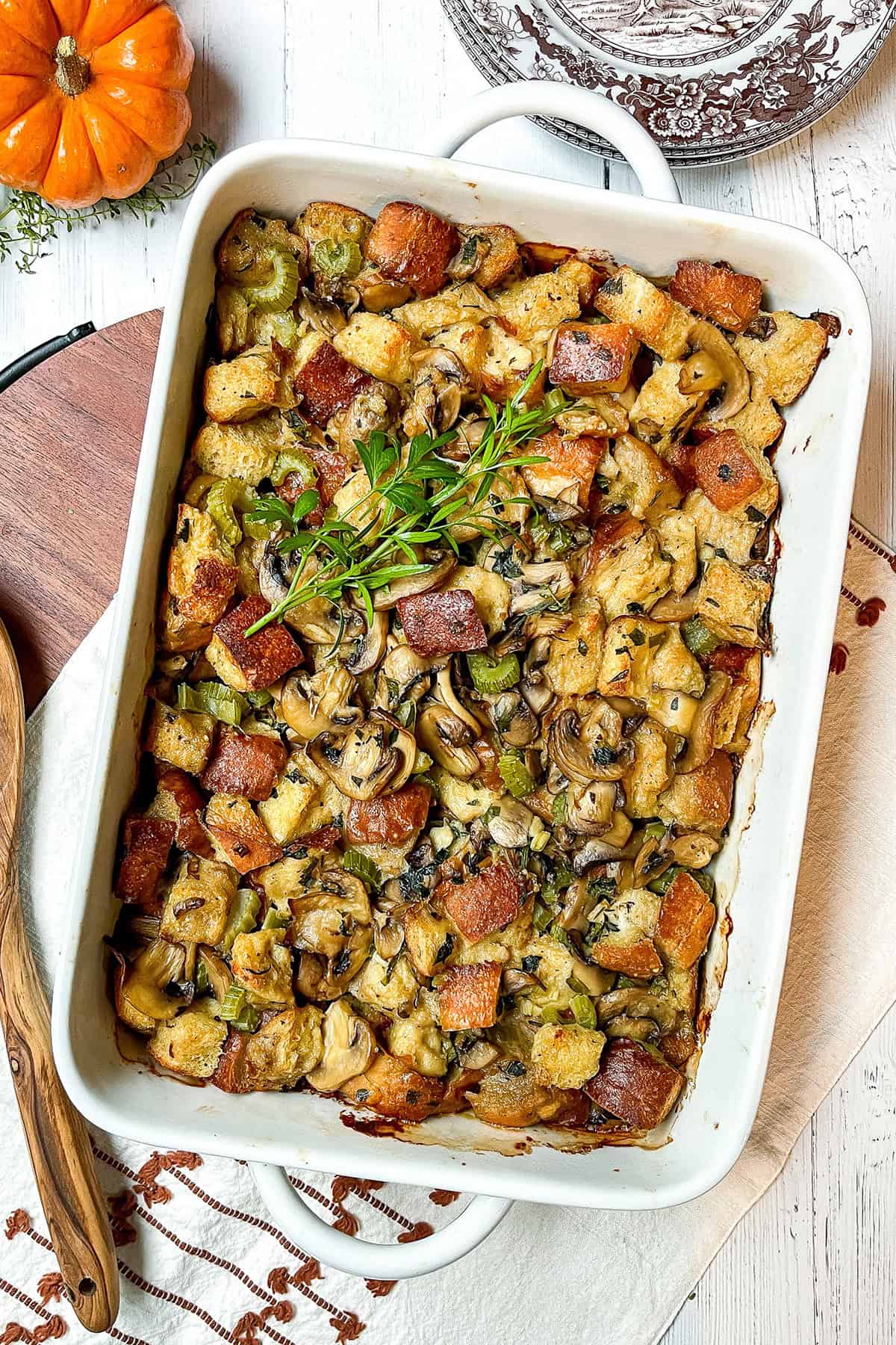 Baked Wild Mushroom Stuffing in a casserole dish with a wooden spoon laying nearby.