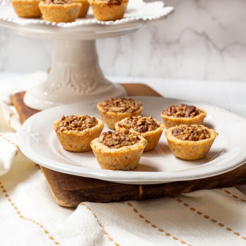 Side view of pecan tassies on a white scalloped plate