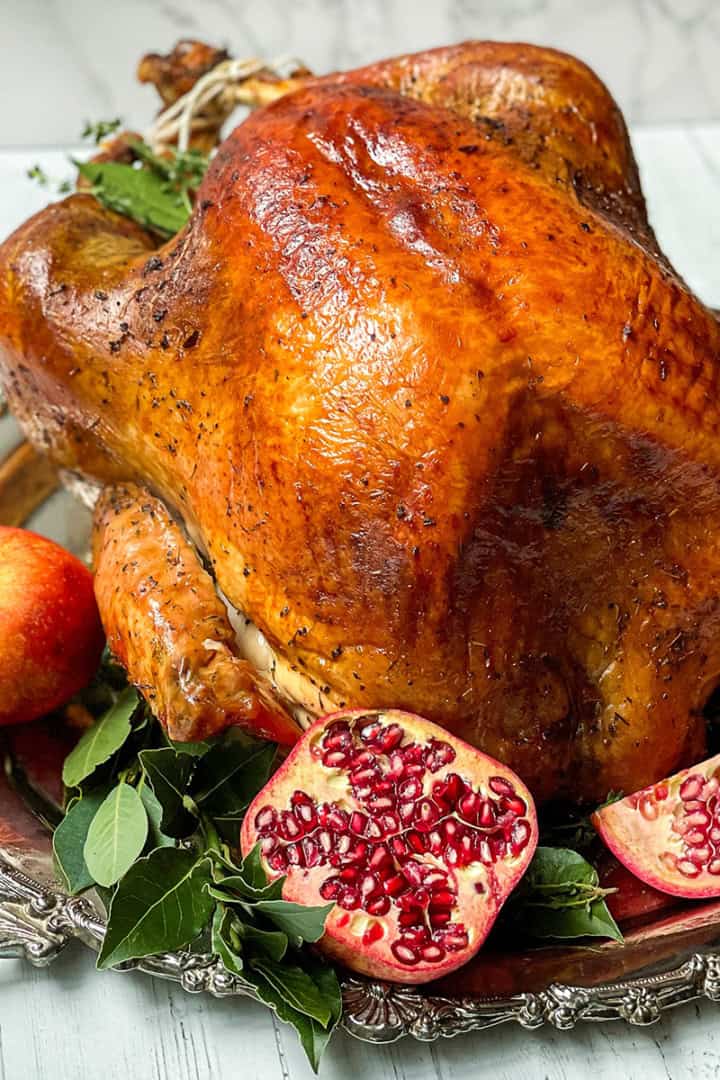 Square image of herb roast turkey on a silver platter with apples, bay leaves, and cut pomegranates.