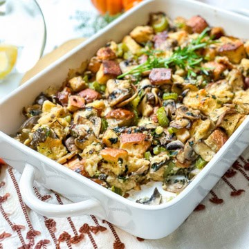 Square image wild mushroom stuffing with a bite missing in a white casserole dish.