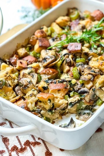 Square image wild mushroom stuffing with a bite missing in a white casserole dish.
