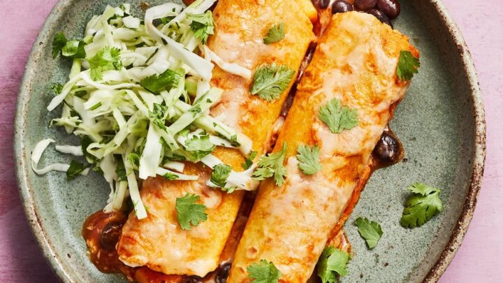 A plate with two enchiladas topped with melted cheese, served with black beans, shredded cabbage, and cilantro garnish—perfect for healthy December dinners.