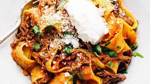 A white bowl filled with pappardelle pasta topped with shredded meat, tomato sauce, grated cheese, fresh herbs, and a dollop of ricotta—a cozy choice inspired by popular healthy dinners.