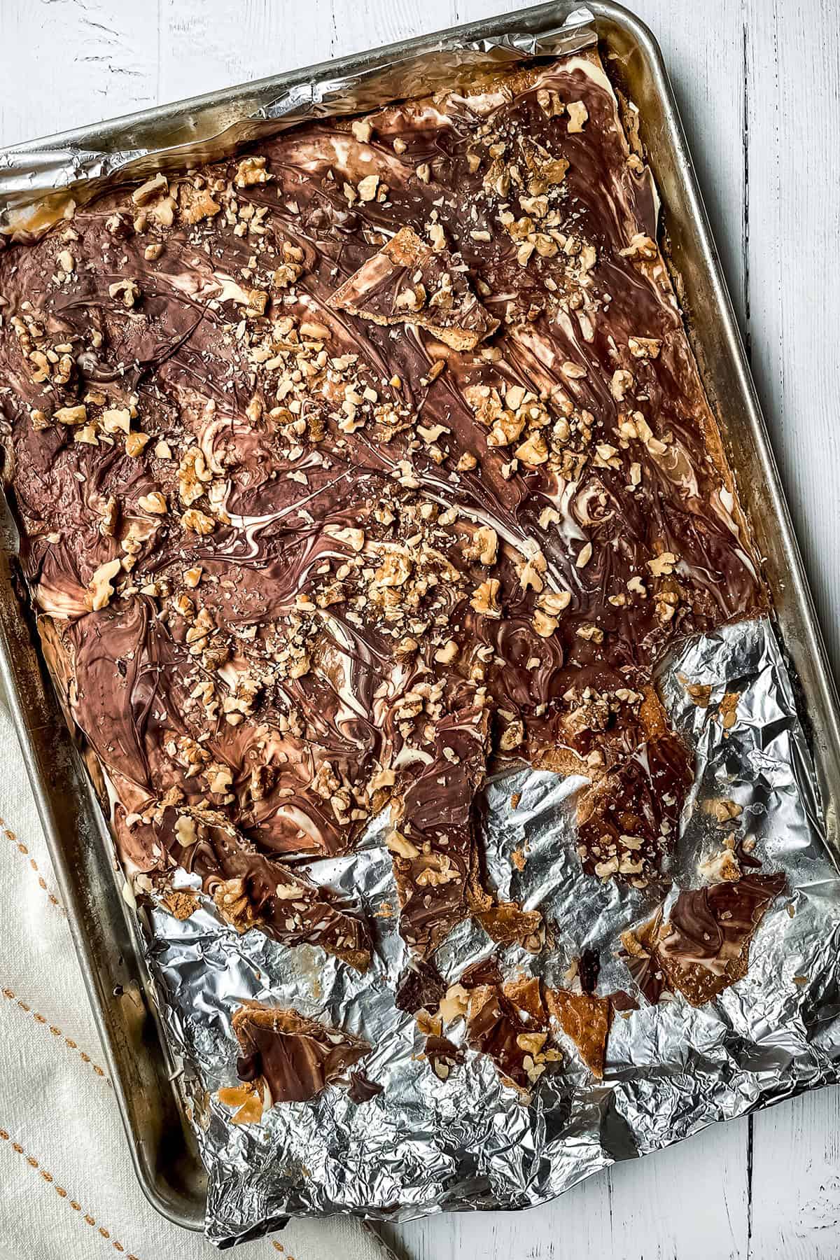 Toffee chocolate crack cooled on a foil lined baking sheet, being broken into pieces.