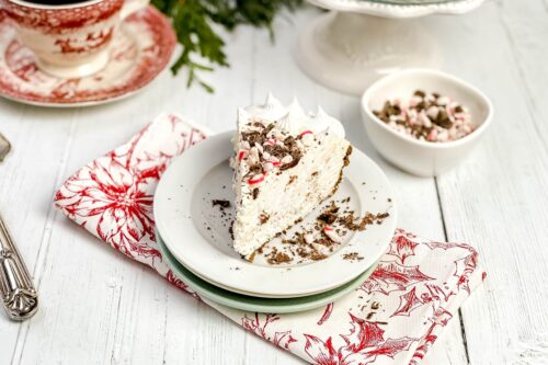 Slice of Peppermint No Bake Cheesecake on a white plate with crushed candy cane and chocolate