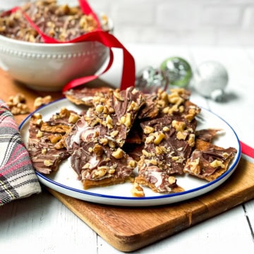 Square image of chocolate crack served on a white plate with more in the background and decorated with a red ribbon.