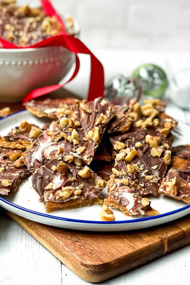 Square image of chocolate crack served on a white plate with more in the background and decorated with a red ribbon.