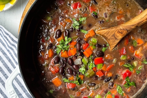 Top view of cooked Black Bean Soup in a Dutch oven with a wooden serving spoon