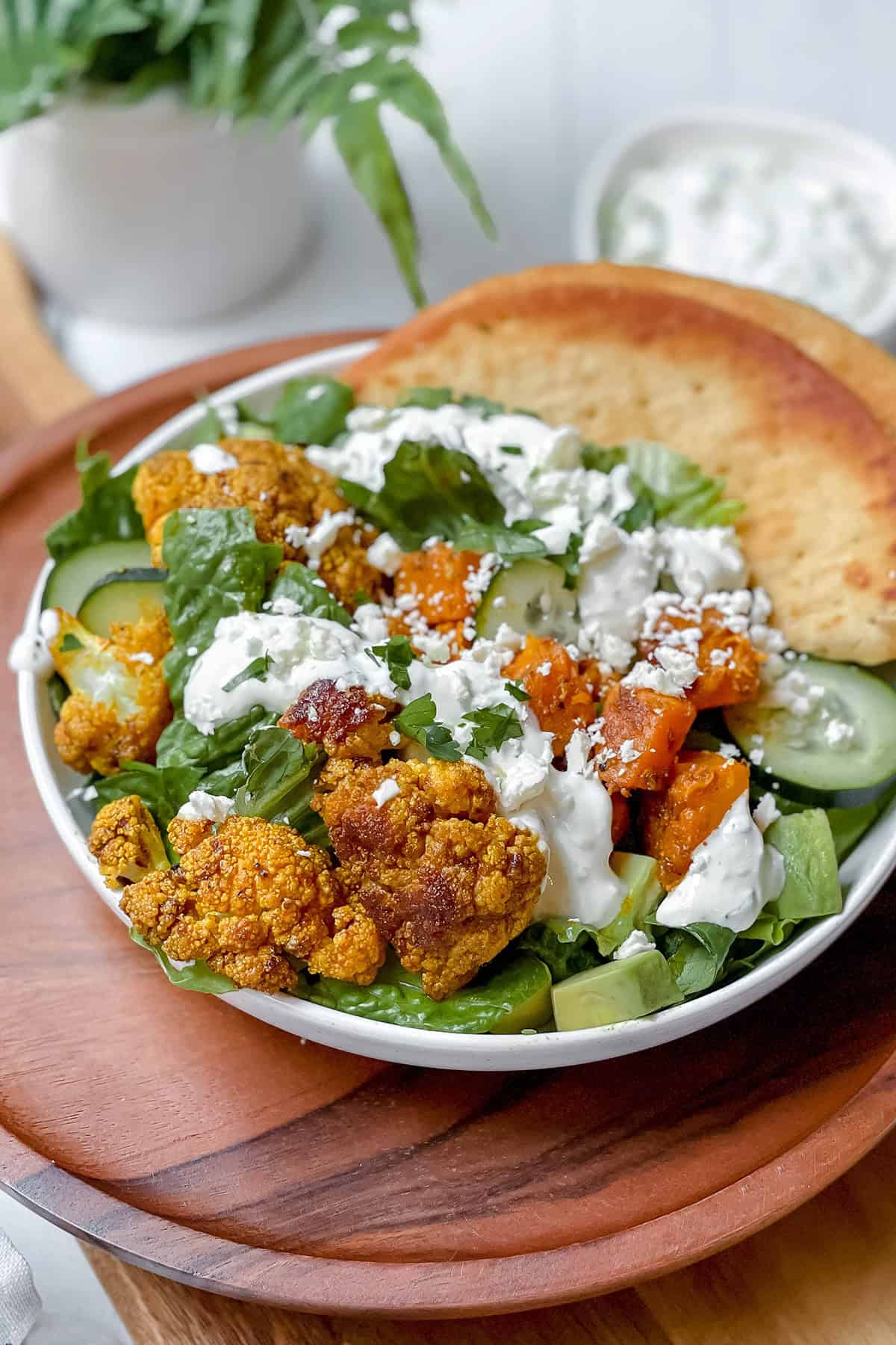 Roasted Cauliflower Bowls smothered in tzatziki sauce with greens, cucumbers, and sweet potatoes.