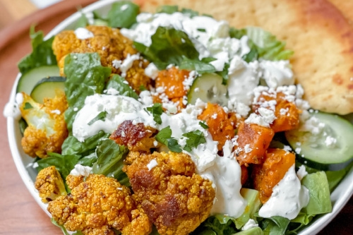 Closeup view of roasted cauliflower with butternut squash, cucumbers and lettuce served with whole grain pitas.