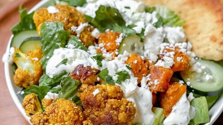 Closeup view of roasted cauliflower with butternut squash, cucumbers and lettuce served with whole grain pitas.