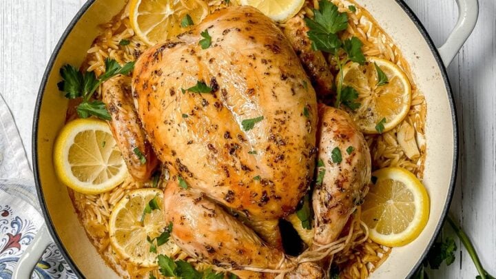 Top view of Greek Roasted Chicken with Lemon Orzo, fresh parsley and feta in a roasting pan.