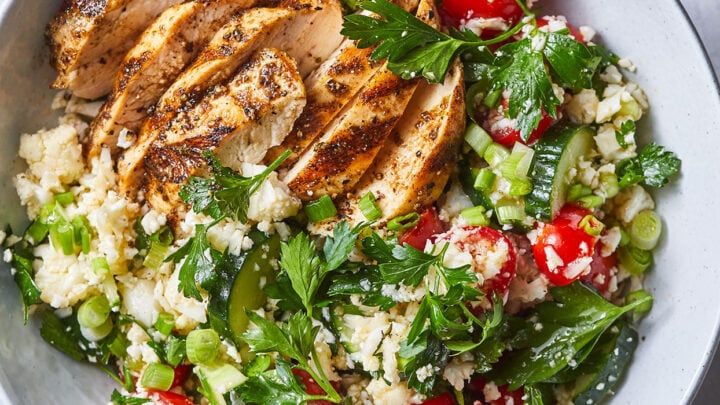 A bowl with sliced grilled chicken breast on a bed of cauliflower rice, cherry tomatoes, cucumber, green onions, and fresh parsley makes a flavorful choice for anti inflammatory dinners.