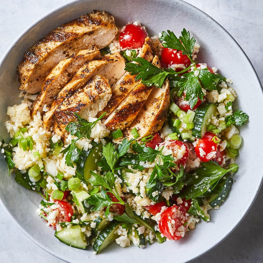 A bowl with sliced grilled chicken breast on a bed of cauliflower rice, cherry tomatoes, cucumber, green onions, and fresh parsley makes a flavorful choice for anti inflammatory dinners.