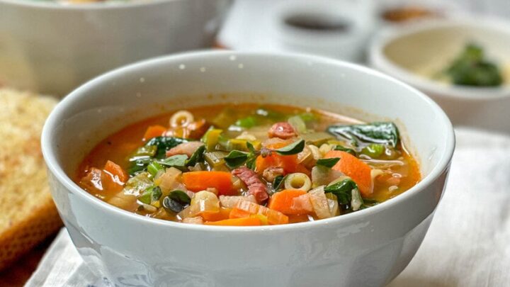 Side view of Italian Minestrone Soup in a white bowl on a rustic wood serving board.