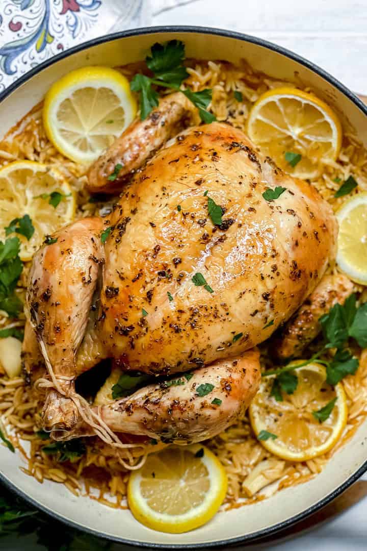 Whole roasted chicken garnished with parsley and lemon slices, served on a bed of rice in a round white dish—a classic roasted chicken meal perfect for any gathering.