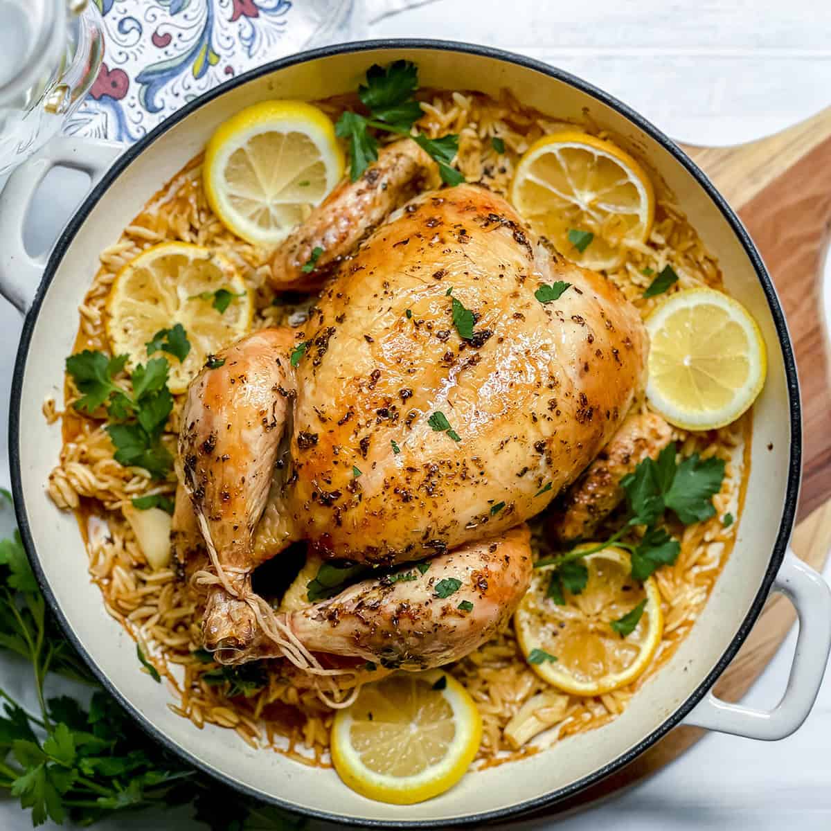 Whole roasted chicken garnished with parsley and lemon slices, served on a bed of rice in a round white dish-a classic roasted chicken meal perfect for any gathering.