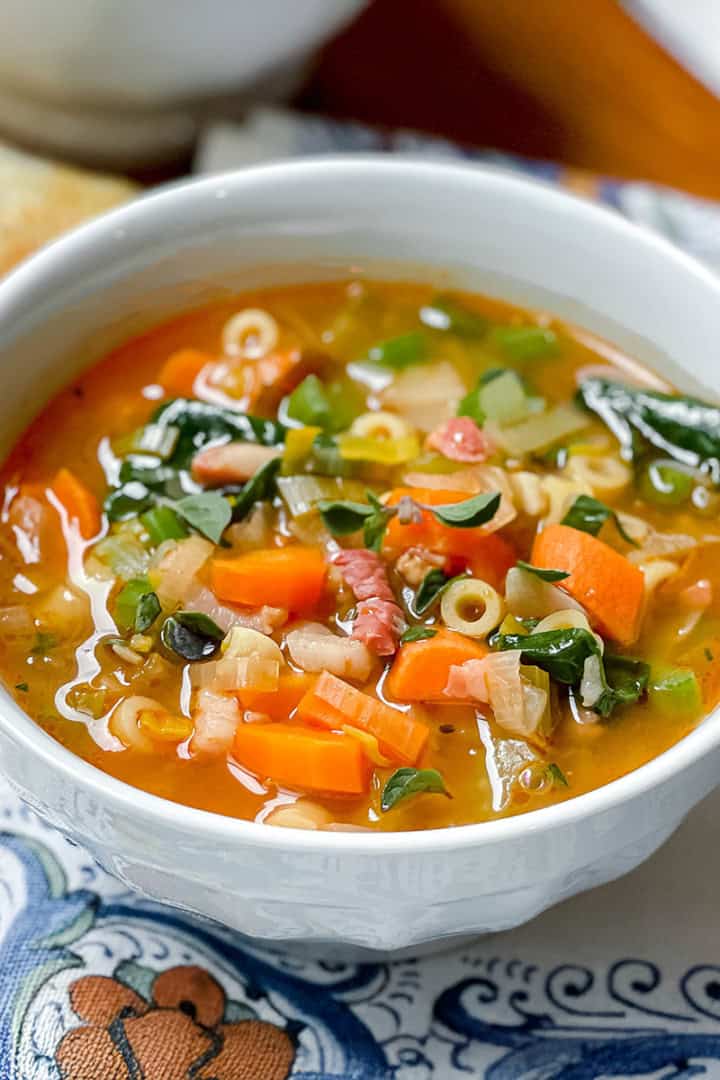 Square image of Italian Minestrone Soup with Crispy Pancetta in a white bowl with vegetables and greens.
