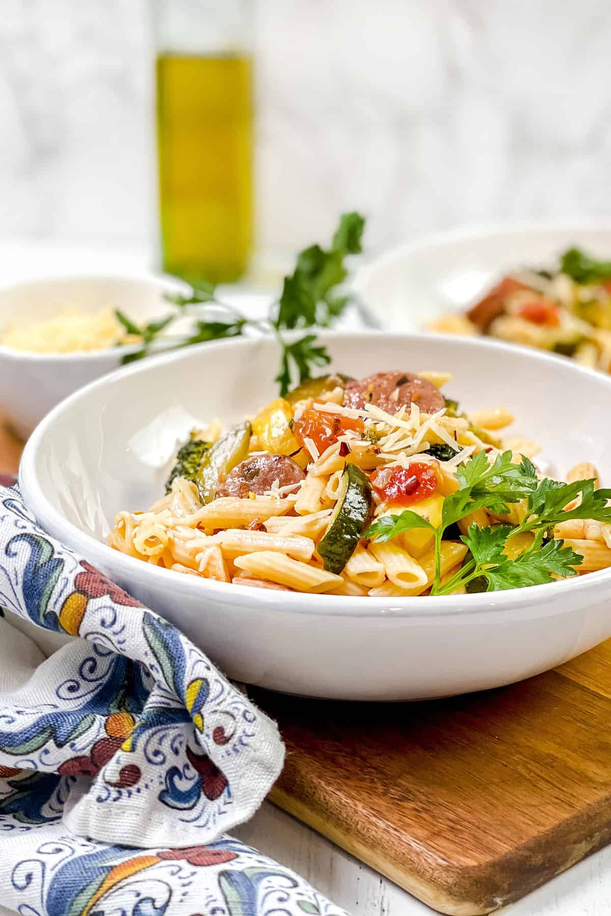 Bowl of Sausage Pasta with fresh parsley garnish sitting on a wooden serving board with more in the background.