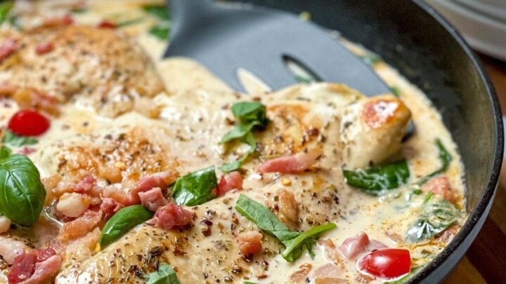 Closeup side view of Tuscan Chicken in a black skillet with a nonstick spatula.