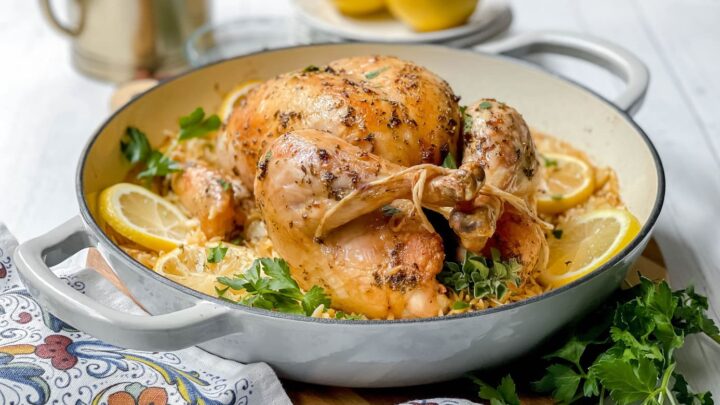 Whole roasted chicken, perfectly seasoned with herbs and garnished with lemon slices, served in a white casserole dish with fresh parsley—a classic roasted chicken that's both flavorful and inviting.