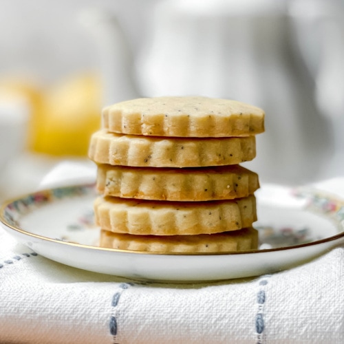 Side view of stacked Lemon Poppy Seed Shortbread Cookies with a white teapot in the background