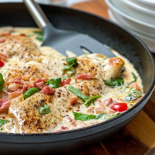 Closeup view of Creamy Tuscan Chicken Skillet with fresh basil and roasted tomatoes.