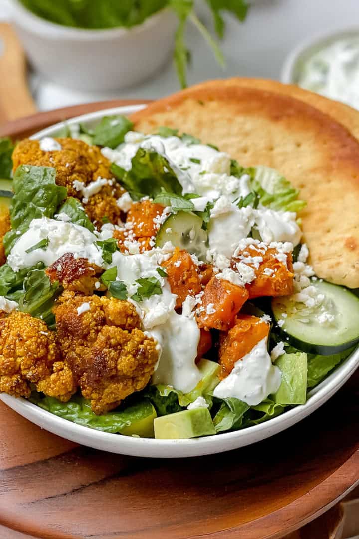 Square image of roasted cauliflower and sweet potato bowl ready for serving with whole grain naan on the side.