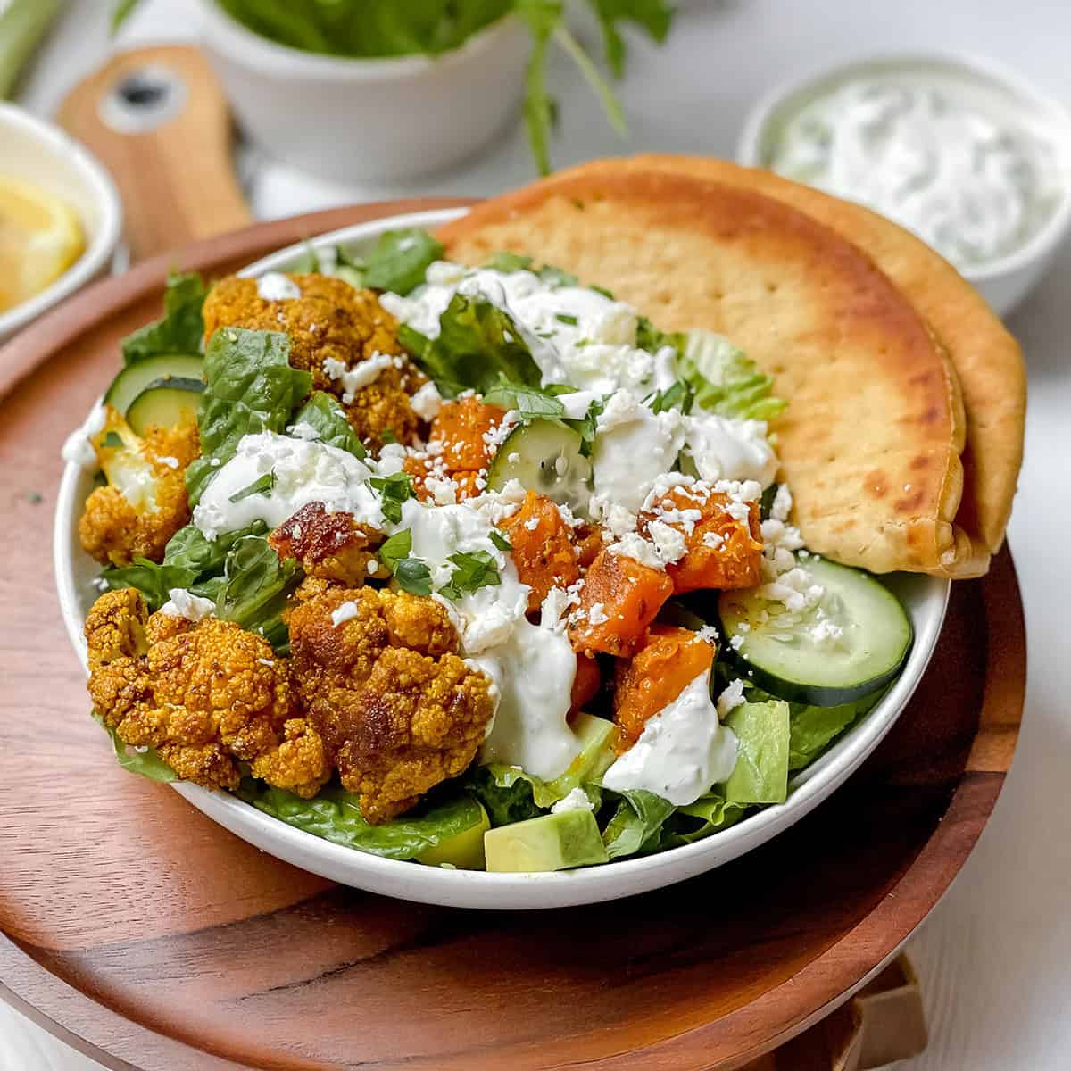 Square image of roasted cauliflower and sweet potato bowl ready for serving with whole grain naan on the side.
