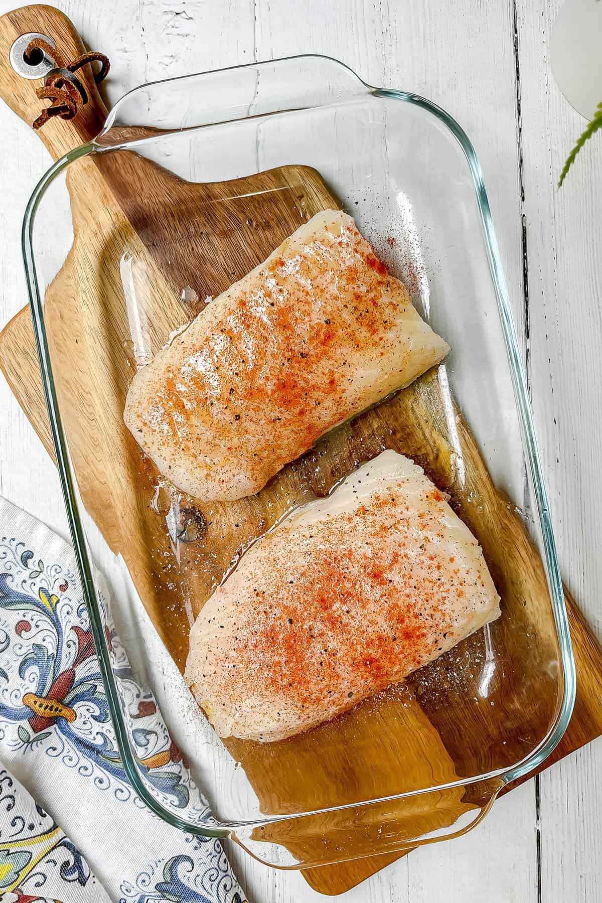 Uncooked seasoned cod fillets in a glass casserole dish ready for baking.