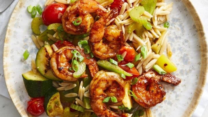 A plate of orzo pasta mixed with sautéed shrimp, zucchini, cherry tomatoes, and celery, topped with sliced green onions—perfect for cozy February One Pot Dinners.