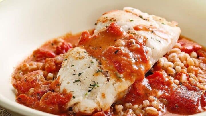 A fillet of white fish served over a bed of grains, topped with chunky tomato sauce in a shallow white bowl—perfect for quick, Under 30 Minute Dinners.