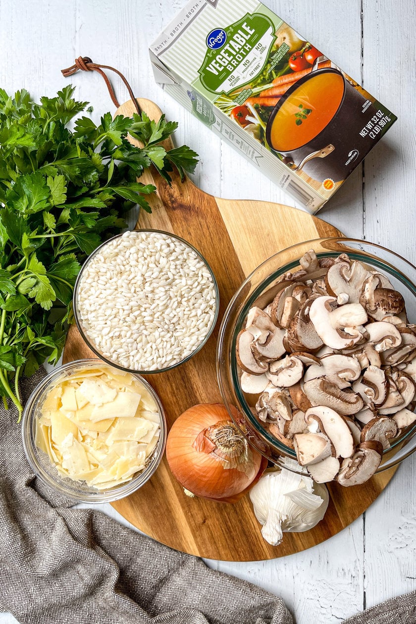 Top view of fresh ingredients for mushroom risotto on a round wood board