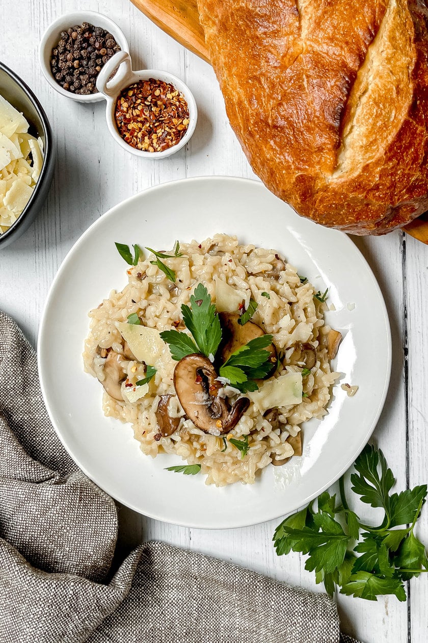 Top view of Mushroom Risotto on a white plate with sourdough bread and shaved parmesan