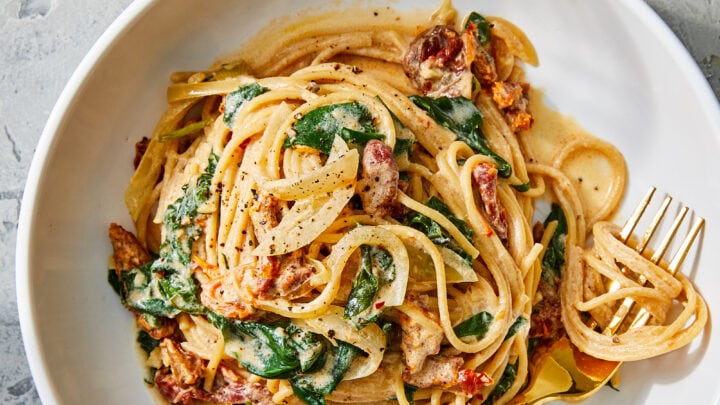 A plate of creamy pasta with spinach and sun-dried tomatoes, served with a fork on a white dish—perfect for Under 30 Minute Dinners.