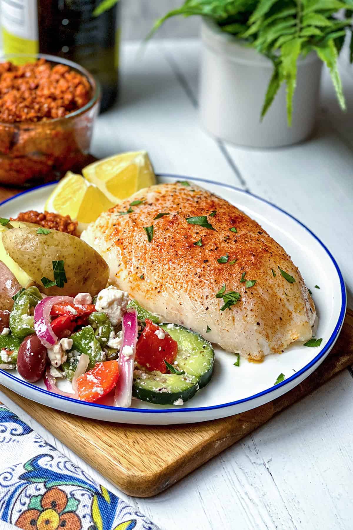 This 15-minute Spanish Baked Cod is garnished with paprika and chopped herbs, served on a plate with mediterranean salad and lemon wedges.