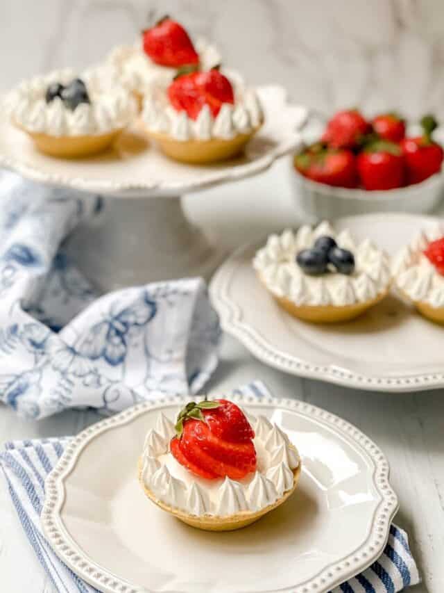 Side view of No Bake Mini Cheesecakes on white plates garnished with fresh fruit and whipped topping