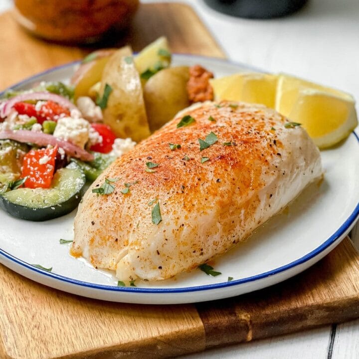 Side view of Spanish Baked Cod on a blue and white plate with lemon wedges