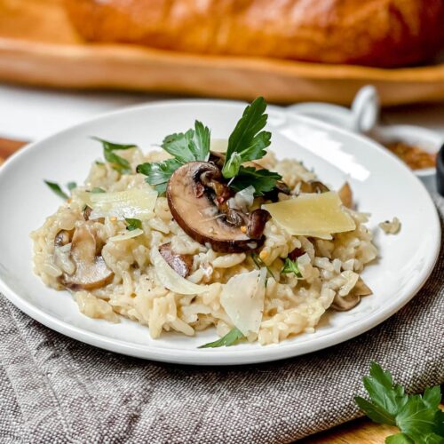 Side view of Mushroom Risotto with fresh parsley and shaved parmesan on a white plate