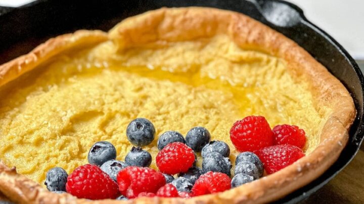 Side view of oven pancake in a cast iron skillet with fresh berries ready for serving