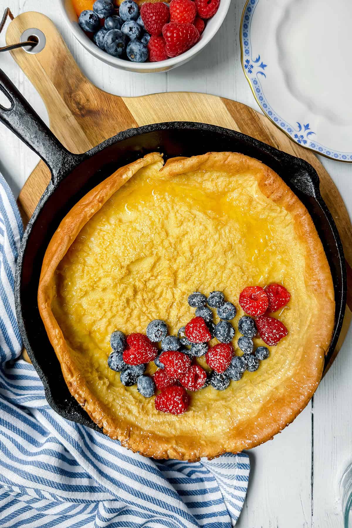 Baked German Pancake in a black cast iron skillet resting on a striped linen and topped with fresh berries ready for serving.