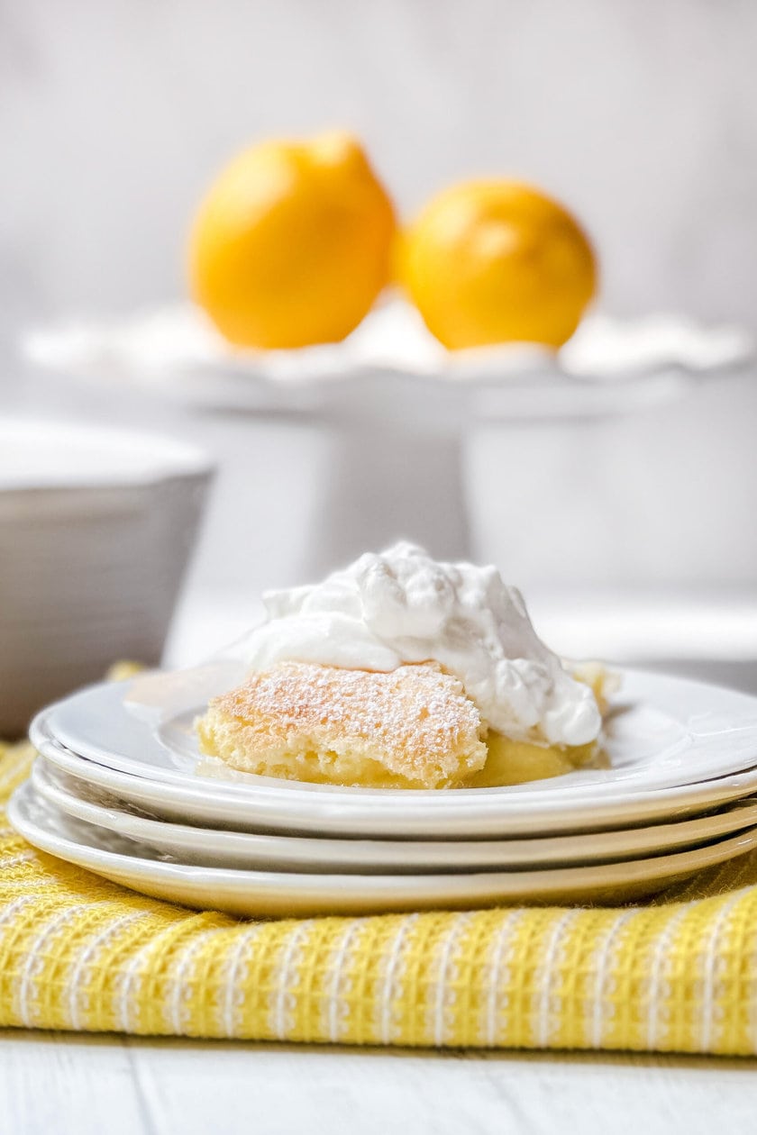 Side view of lemon pudding serving on a white plate topped with freshly whipped cream