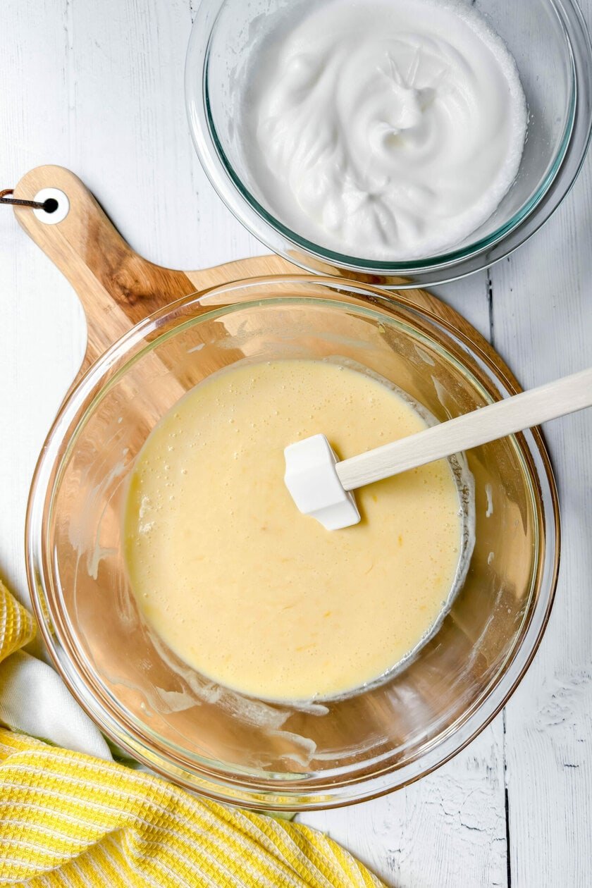 Top view of lemon pudding batter in a glass bowl with a whipped egg whites in a separate bowl