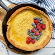 Square image of baked German Pancake in a cast iron skillet topped with fresh blueberries and raspberries.