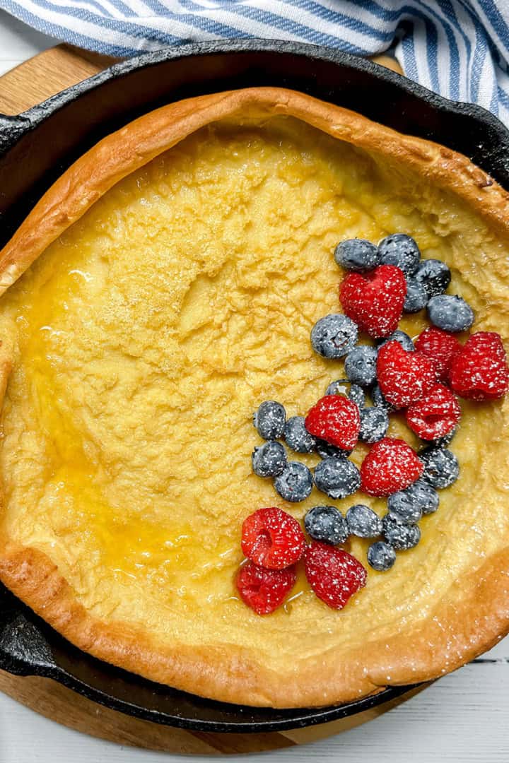 Square image of baked German Pancake in a cast iron skillet topped with fresh blueberries and raspberries.