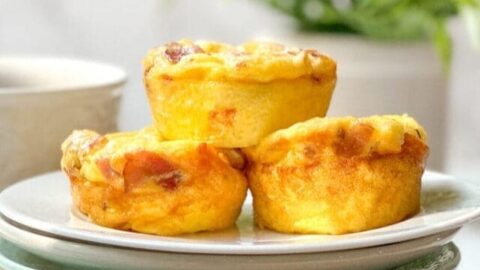 Side view of 3 Bacon Gouda Egg Bites on a white plate with coffee