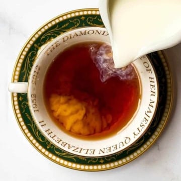 Cream being poured into Irish Breakfast Tea served in a Queen Elizabeth Jubilee teacup.